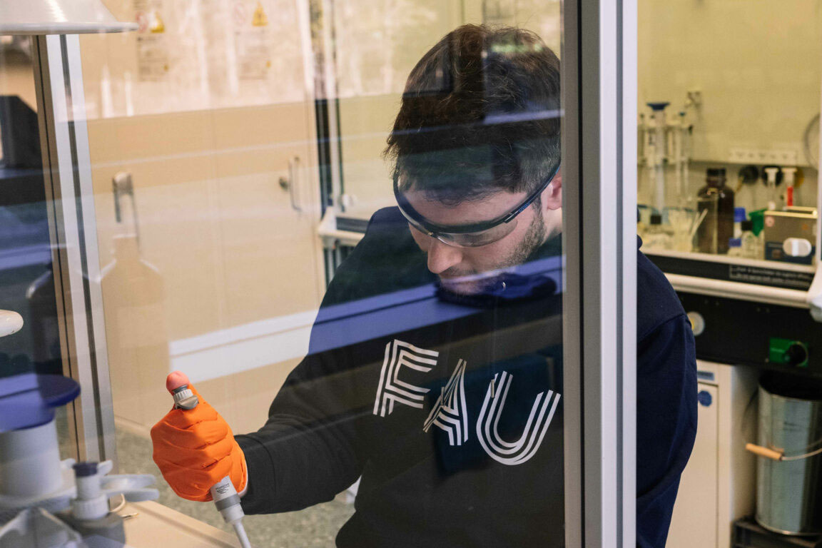 Forscher mit Schutzbrille und FAU-Pullover im Labor.