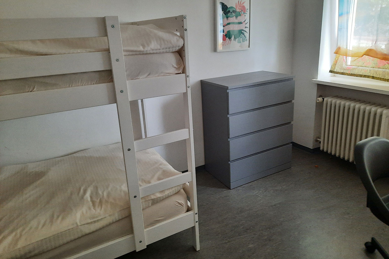 View of a dormitory with dresser and bunk beds.