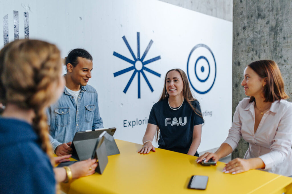 Several people are seated at a table with mobile devices and laptops.