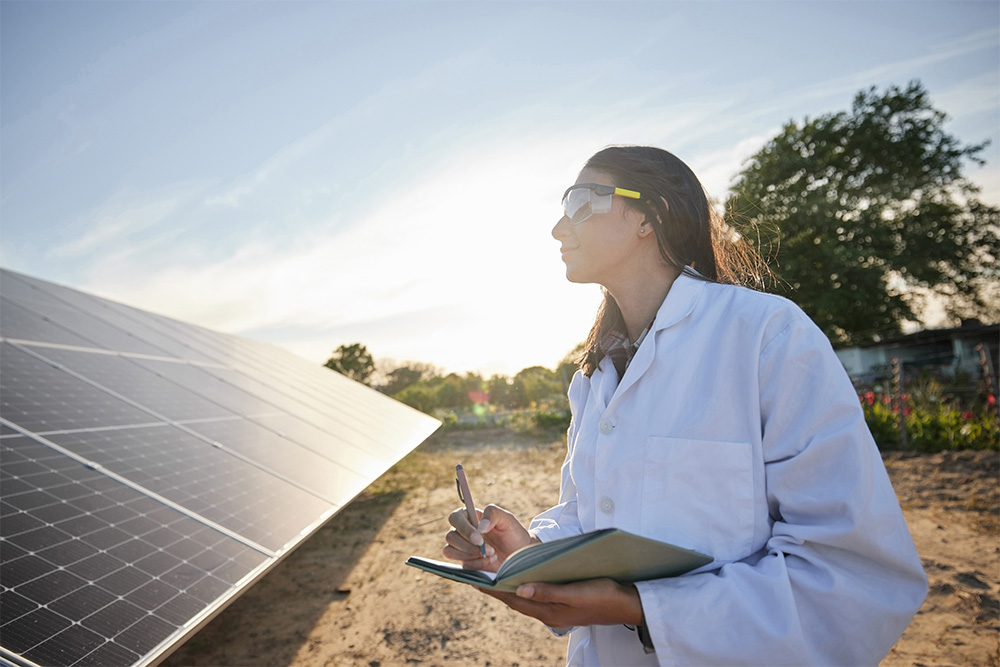 Eine Frau mit Laborkittel steht auf einem Feld mit Solarpanels.