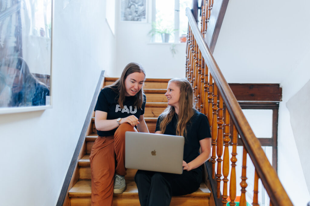 Zwei Studierende sitzen mit einem Laptop auf einer Treppe.