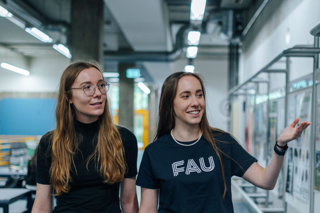 Two women walking down a corridor talking to each other.