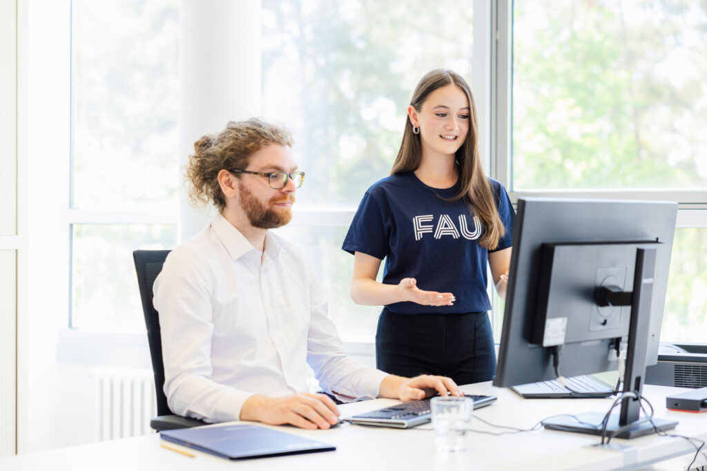 Eine Frau spricht mit einem Mann vor dem PC