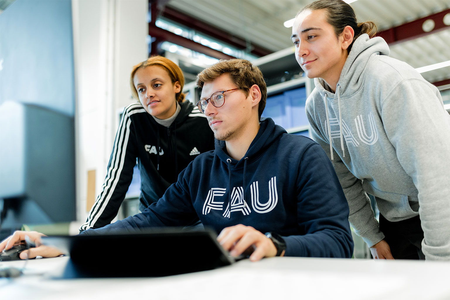 Drei Forschende arbeiten gemeinsam am Computer. Einser sitzt, die anderen stehen dahinter.